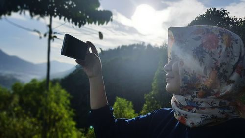 Woman wearing headscarf photographing against mountain