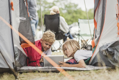 Siblings talking while using digital tablet in tent at campsite