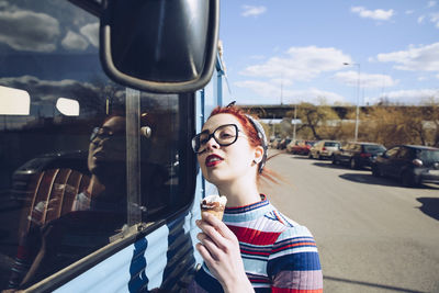 Young woman holding ice cream cone while standing by mini van on street