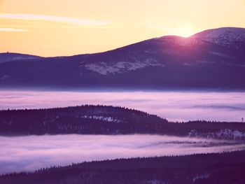 Pink orange sun rise above misty winter mountains. peaks of mountains above creamy mist in valley.