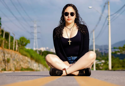 Young woman wearing sunglasses sitting against sky