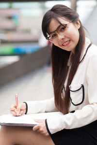Portrait of young businesswoman writing while sitting on steps
