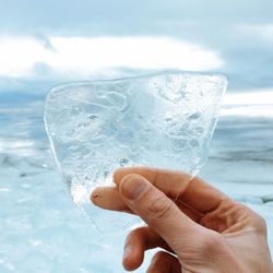 Close-up of hand holding ice against sky