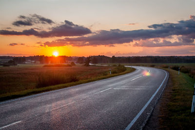 Road by landscape against sky during sunset