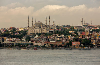 Strait by buildings and mosques against cloudy sky