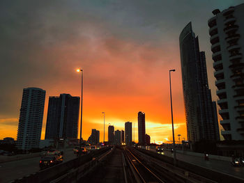 Cars on road by buildings against sky during sunset