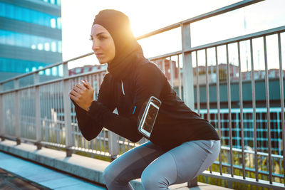 Beautiful woman wearing hijab exercising against building during sunrise