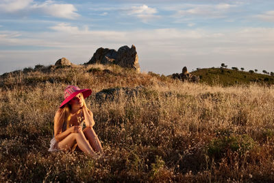 Young woman sitting on grass against sky