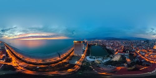 Panoramic shot of illuminated cityscape against sky during sunset