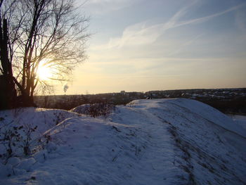 Snow covered landscape against sky during sunset