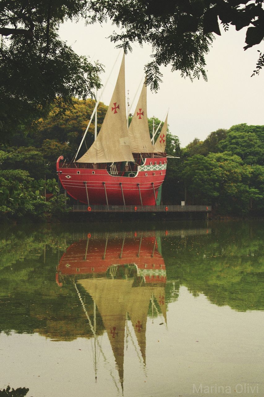 water, reflection, tree, nautical vessel, waterfront, lake, transportation, plant, nature, mode of transportation, no people, day, sky, outdoors, tranquility, architecture, built structure, symmetry, sailboat