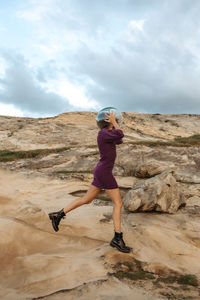 Side view female dreaming of being astronaut and jumping in glass helmet on rocky terrain near sea