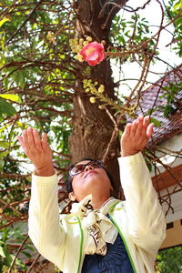 Low angle view of woman gesturing below flower on branch