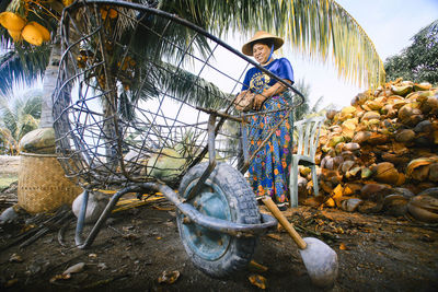 Full length of woman holding coconut while standing by cart on land