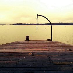 Bench by lake against sky during sunset