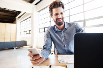 Portrait of young man using phone while sitting on table