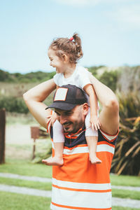 Smiling man carrying daughter while standing against sky