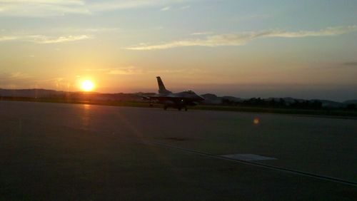 Airplane flying over airport runway against sky during sunset