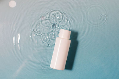 Bottle of cosmetic product with space for text on blue surface with clear water