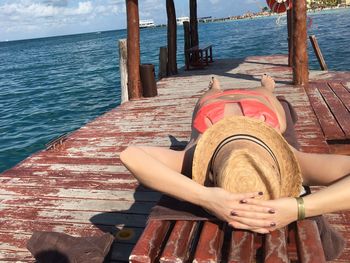 Low section of woman sitting on wooden post against sea