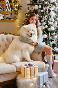 Little cute girl sitting on the sofa with samoyed dog