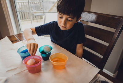 Boy making easter eggs on table while sitting at home