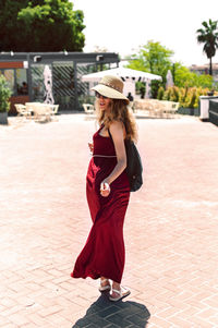 Full length of woman wearing hat and red dress on street during sunny day