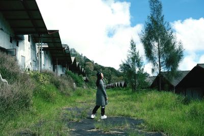 Full length of woman standing on field by houses against sky