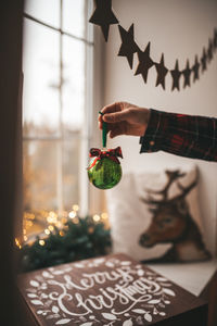 Cropped hand of person holding christmas decoration at home