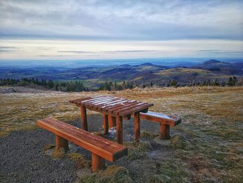 Empty bench on field by mountains against sky