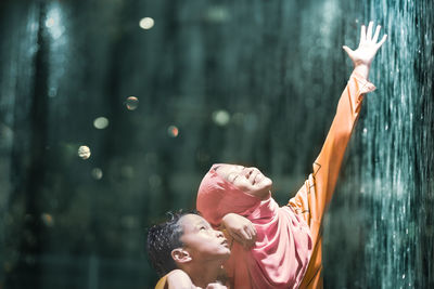 Teenage girl with brother by artificial waterfall