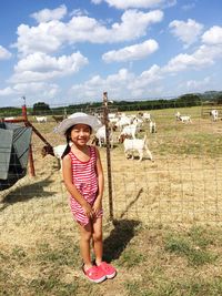 Full length of happy girl standing against goats at farm