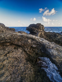 Rock formation on sea shore against sky