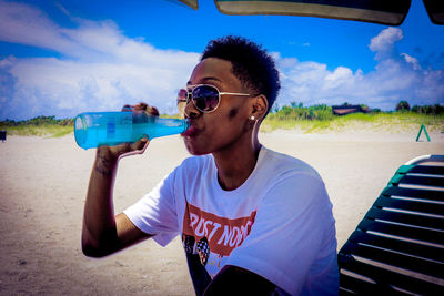 Young man wearing sunglasses on beach against sky