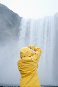 Rear view of young woman standing against waterfall