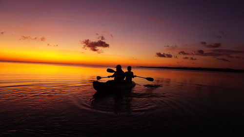 Silhouette people rowing boat in sea against sky during sunset