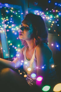 Woman sitting by illuminated multi colored lights