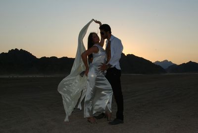 Full length of young man and woman standing at desert against sky