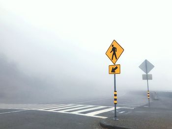 Road sign against clear sky during foggy weather