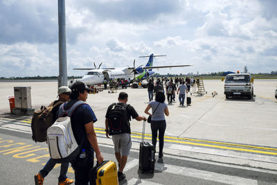 Group of people on airport runway against sky