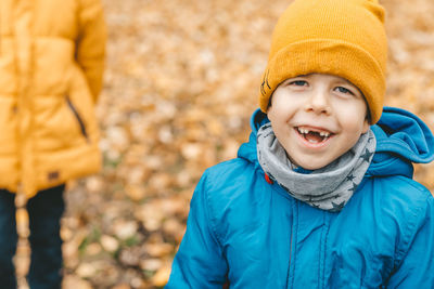 Portrait of a smiling boy in a hat and a blue jacket, outdoors, against a background of yellow leave