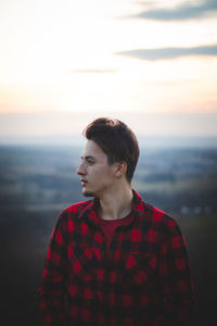 Candid portrait of a man in his 20s dressed in a black and red checked shirt looking into his future