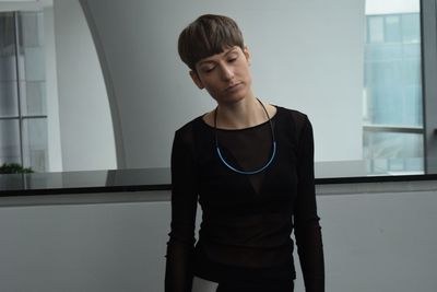 Young woman looking down while standing against window