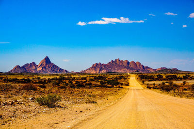 Dirt road leading towards rocky mountains against sky