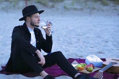 Side view of young man drinking wine on the beach