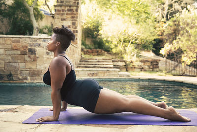 Profile view of determined woman doing push-ups on mat at poolside