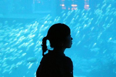 Girl standing against fishes at aquarium