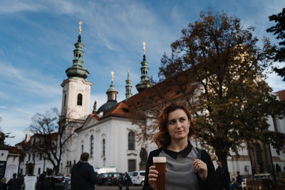 Woman holding beer against building in city