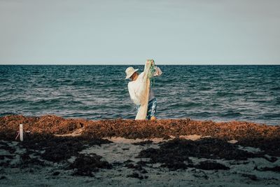 Rear view of woman standing at beach against sky