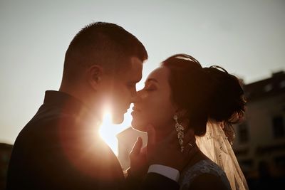 Close-up of bride and bridegroom kissing against clear sky